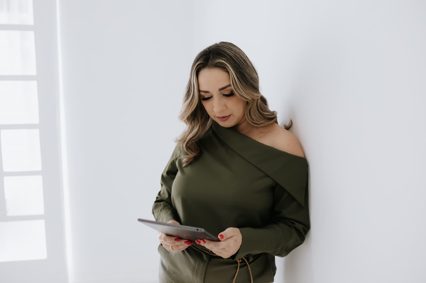 Edkarla Almeida lendo em um tablet, encostada em uma parede branca